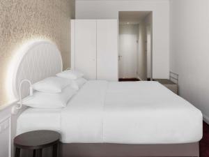 a white bedroom with a white bed and a stool at Hotel Rathauspark Wien - Handwritten Collection in Vienna
