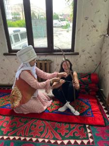 two women sitting on a bed playing a instrument at Guest House URUYAT in Naryn