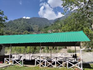 a green roofed picnic shelter with mountains in the background at Ambika Campaign Huts in Manāli +1 photo