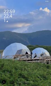 two domes on a hill with people standing in them at AK chatyr in Tong