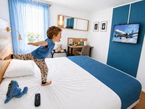 a young child jumping on top of a bed at The Originals City, Hôtel Mâcon Sud in Chaintré