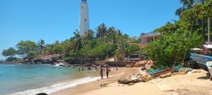 a beach with a light house and people on the beach at Lighthouse Peacock Villa in Dondra West +9 photos
