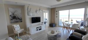 a living room with a couch and a tv and a table at Dolphin Beach H203 Table Mountain Views in Bloubergstrand +25 photos