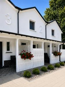 a white house with red flowers in the windows at Domki Magnolia - komfortowe domki dla rodzin nad morzem in Dźwirzyno