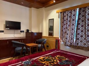 a room with a bed and a table and a television at The Juniper Ladakh Guest House in Kargil