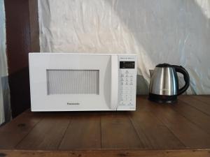 a microwave oven on a wooden table with a coffee pot at Apartamentos do Centrinho do Rosa in Imbituba