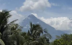 a mountain in the distance with palm trees and clouds at Balay by JMB in Legazpi