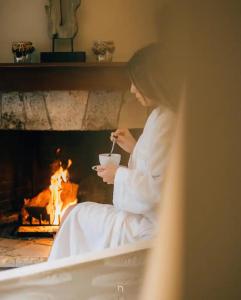a woman sitting in front of a fireplace with a bowl of soup at MARON ΙΙ με τζάκι in Kalavrita