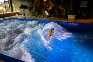a woman riding a wave on a surfboard in a pool at Van Der Valk Luxembourg Arlon in Arlon