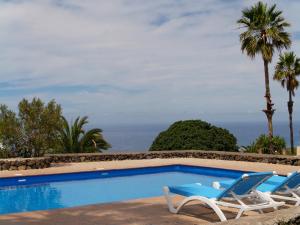 a swimming pool with two chairs and the ocean at Bungalows El Paradiso in Tazacorte