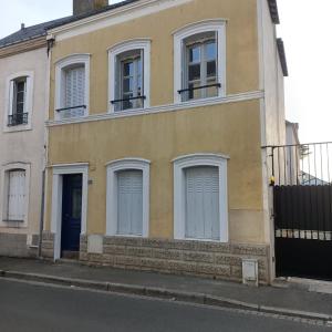 a yellow building with white windows and a blue door at Maison de ville in Évron