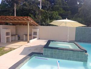 a swimming pool with an umbrella next to a house at Estância Serra Du Capiau 01 in Mairiporã
