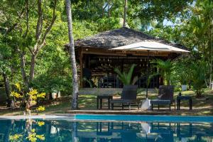 a pavilion with chairs and an umbrella next to a pool at Ecoya Riverside Resort in Balapitiya