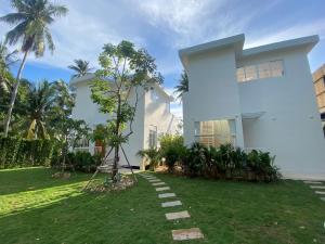 a white house with a grass yard in front of it at Blue Garden Villa A in Ban Madua Wan