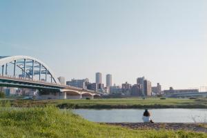 a person sitting on the steps near a river with a bridge at The Aoca Tokyo Kaminoge in Tokyo
