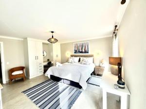 a white bedroom with a bed and a chair at Adrift Guesthouse in St Francis Bay