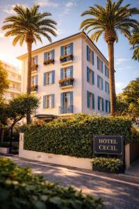 a hotel with palm trees in front of a building at Hôtel de charme CECIL in Juan-les-Pins