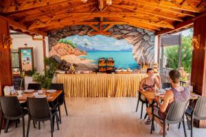 two women sitting at tables in a restaurant with a mural at Palma Rosa Hotel in Kemer