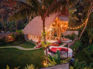 a house with a thatch roof and a palm tree at Bambu Teras Viewpoint in Karangasem