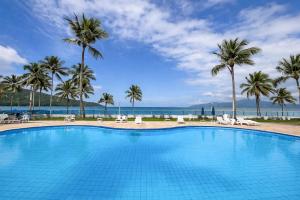 a large swimming pool with palm trees and the ocean at Apto pe na areia 3 dorm ar cond in Caraguatatuba