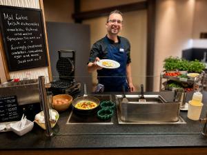 a man standing in a kitchen holding a plate of food at AMBER HOTEL Bavaria in Bad Reichenhall