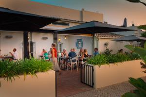a group of people sitting at tables in a patio with umbrellas at Casa Porta Azul in Boliqueime
