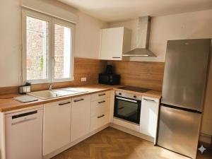 a kitchen with white cabinets and a stainless steel refrigerator at Le passage, maisonnette cosy classée 4 étoiles in Pont-lʼÉvêque