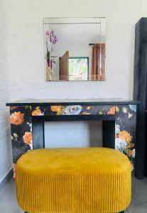 a mirror above a bench with a yellow ottoman at Origin Cottage in eMalahleni