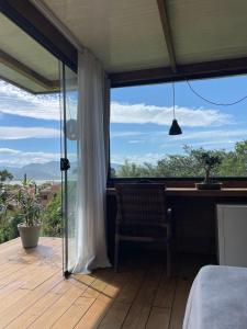 a bedroom with a large window with a bed and a desk at Suítes Âncora Praia do Rosa in Imbituba