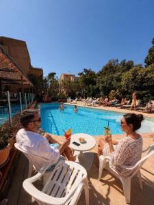 a man and woman sitting at a table by a swimming pool at Hôtel Le Maritime in Argelès-sur-Mer