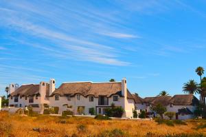 a large white house with palm trees and a blue sky at Shelley Point Townhouse in Stompneusbaai