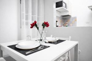 a table with two plates and a vase with red flowers at Le Erbe Apartment tra Locali e vita Universitaria in Genoa