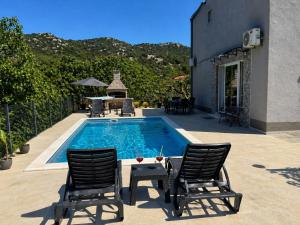 a swimming pool with two chairs and a table next to a house at Apartment Ćulum in Peračko Blato