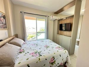a bedroom with a bed with a floral comforter and a window at Apartamento 83 - Carmelo in Ribeirão Preto