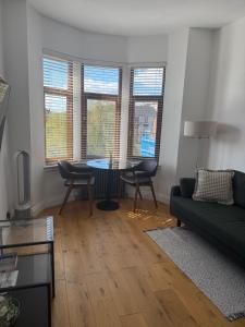 a living room with a couch and a table and windows at Top Floor West End Flat - 3-Min Walk to Subway - Park Views in Glasgow
