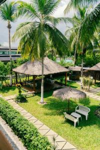 a park with benches and umbrellas and palm trees at Hôtel Touraco in Assinie