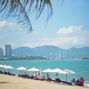 a group of people sitting on a beach with umbrellas at Panorama Blue Beach Nha Trang in Nha Trang