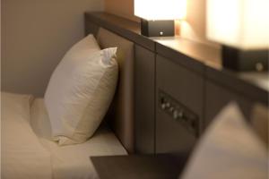 a bed with a white pillow next to a dresser at Hakata Green Hotel Tenjin in Fukuoka