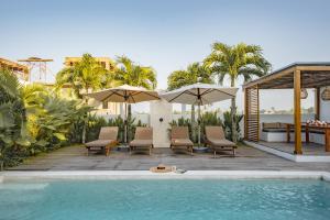 a pool with chairs and umbrellas next to a house at Botanique Villa & Studio in Tanah Lot
