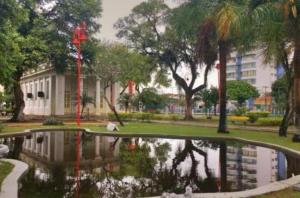 a pond in a park with a reflection of a building at Studio Premium Trianon Centro in Campos dos Goytacazes