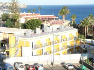 un edificio amarillo con coches estacionados frente al océano en Apartamentos Karina en Playa del Ingles