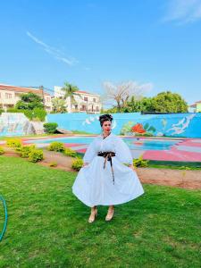 a woman in a white dress standing in the grass at Acomodações e Serviços TR in Maputo