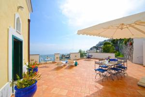 eine Terrasse mit Tischen, Stühlen und einem Sonnenschirm in der Unterkunft Casa Alessia in Praiano