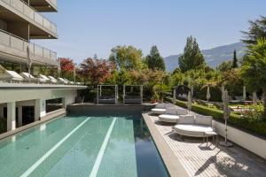 a swimming pool with lounge chairs next to a building at Feldhof DolceVita Resort in Naturno