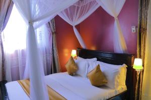 a bedroom with a canopy bed with white sheets and yellow pillows at KH KH Hotel in Kasese
