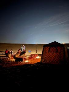 a group of people sitting on a beach next to a tent at Desert Safari in Margham
