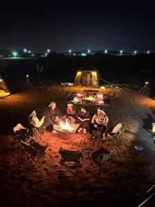 a group of people sitting around a fire in front of a tent at Desert Safari in Margham