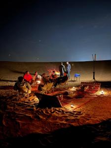 a group of people sitting around a fire on the beach at Desert Safari in Margham