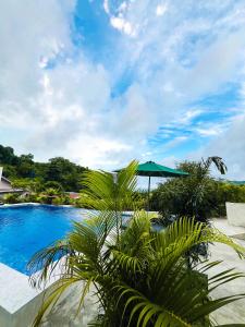 a blue swimming pool with a green umbrella and palm trees at Garden Hill Views in Kuta Lombok