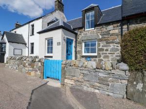 a stone house with a blue fence in front of it at Post Cottage in Arisaig